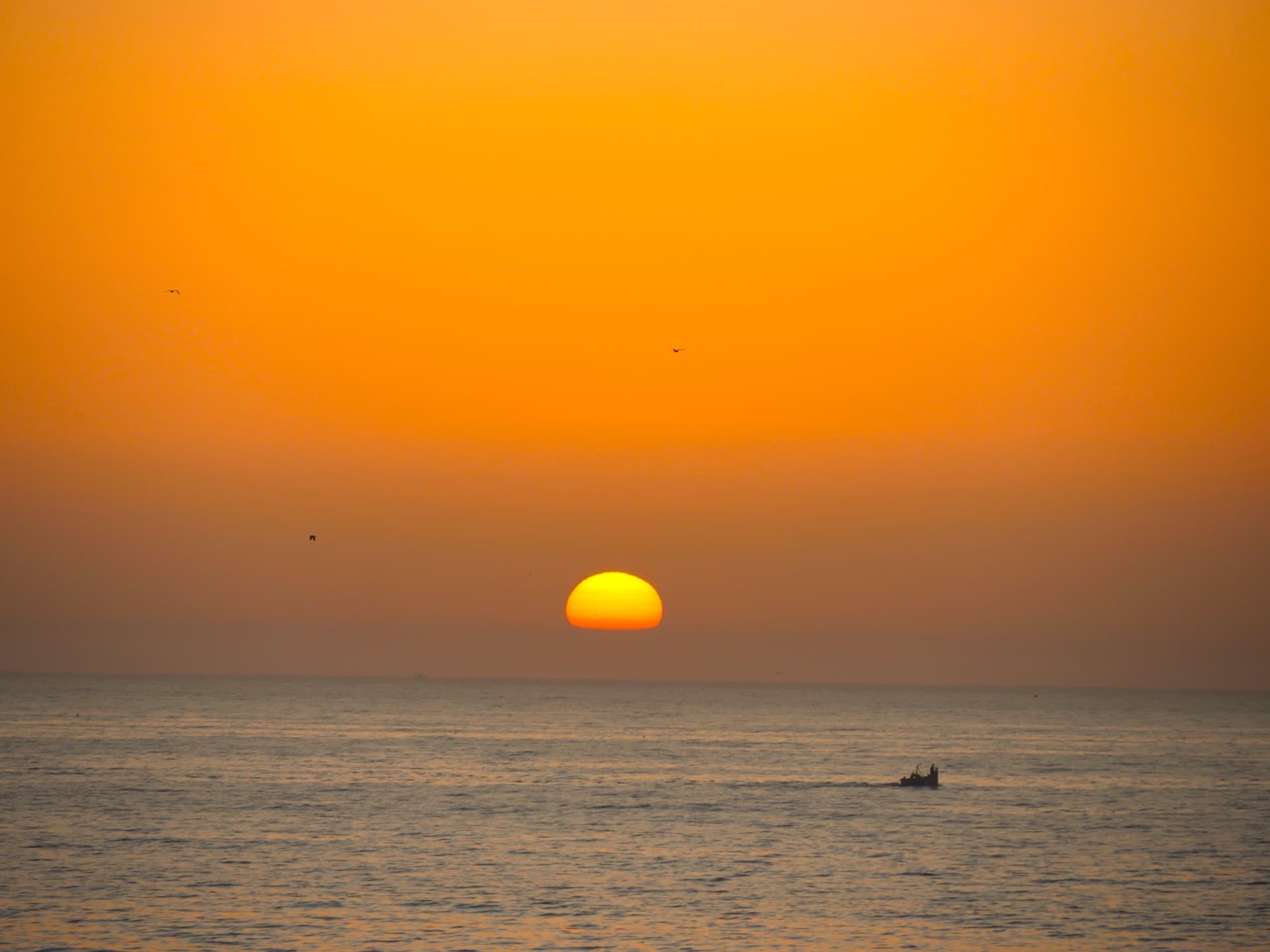 Dramatic orange sunset over the ocean with fishing boat