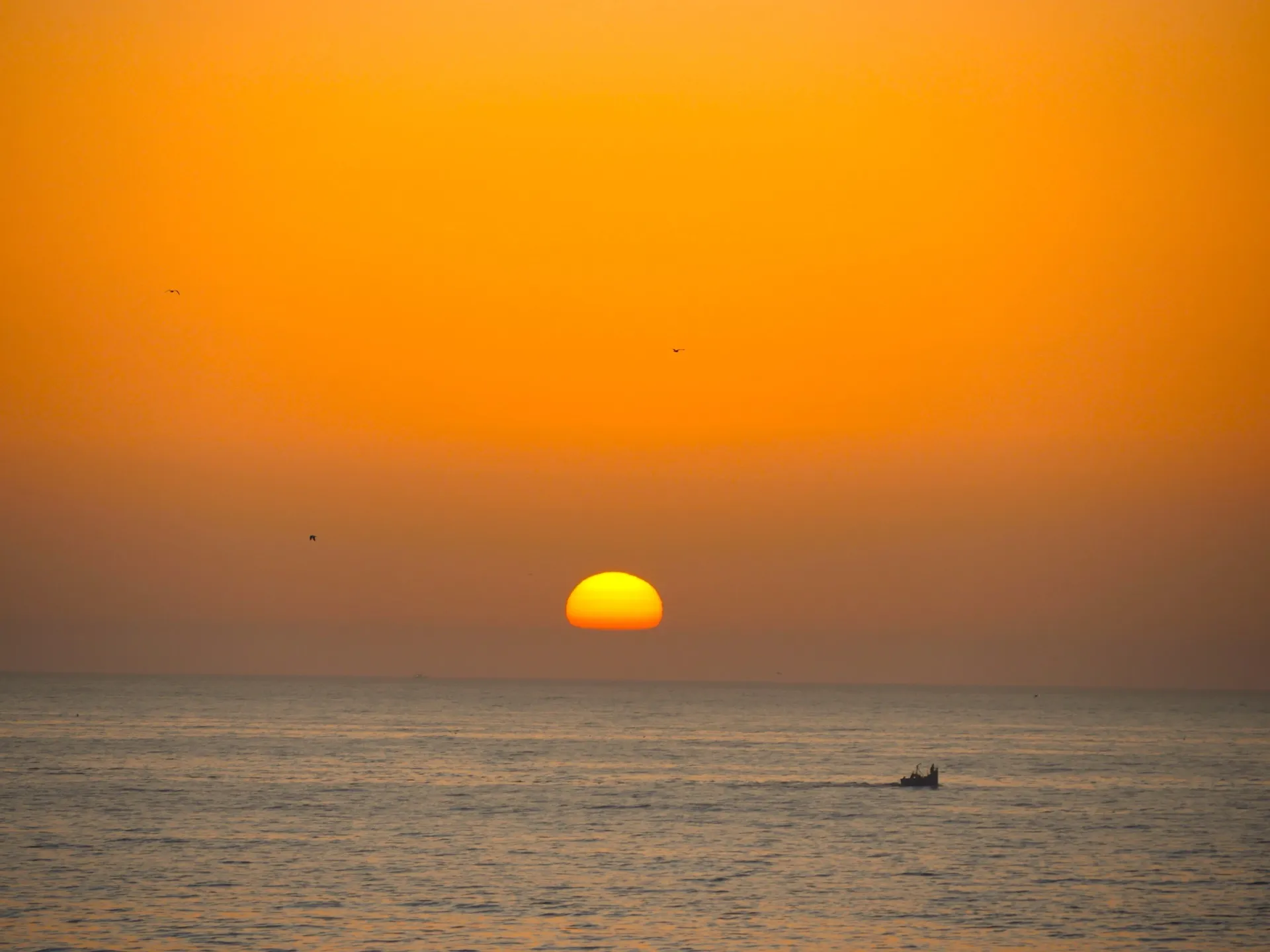 Dramatic orange sunset over the ocean with fishing boat